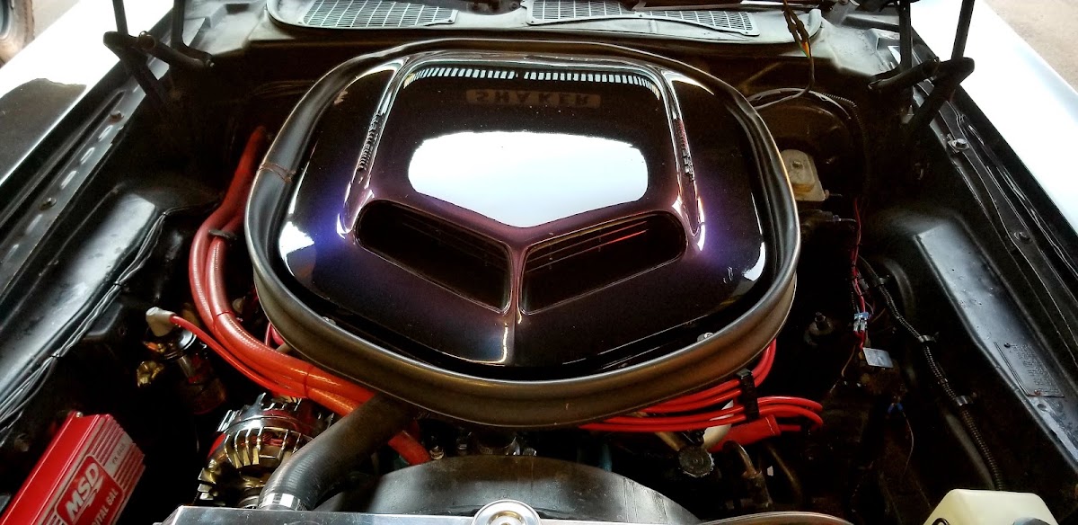 Classic muscle car engine bay with a polished hood scoop and red ignition wires